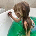 Child writing on a bath with a bath colours 